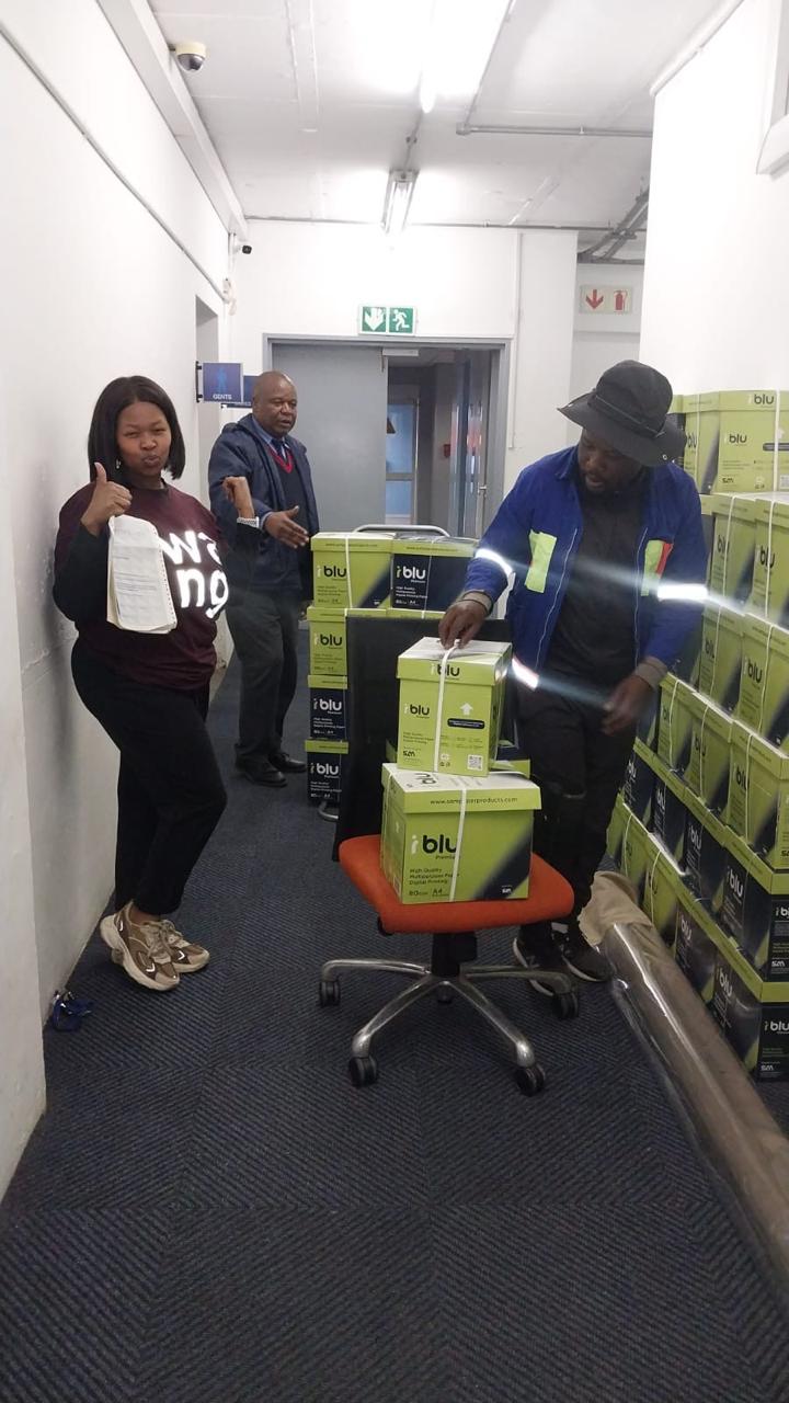 Workers organising boxed supplies inside an office corridor
